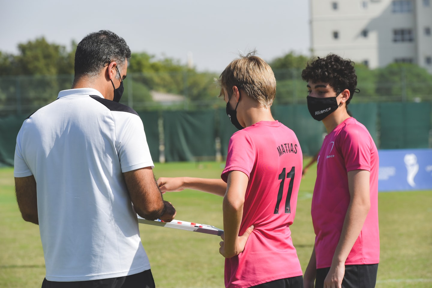 Allenatore spiega agli atleti con una lavagna su un campo da gioco soleggiato.